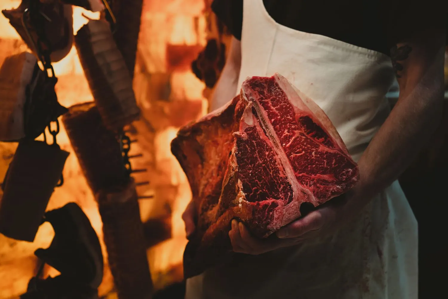 Boucher tenant une côte de bœuf devant des flammes
